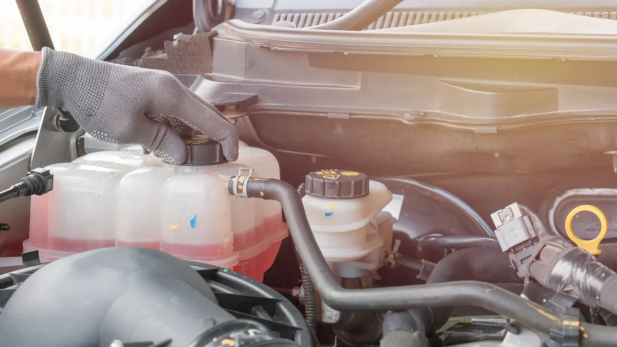 Gloved technician checking the coolant level in an expansion tank