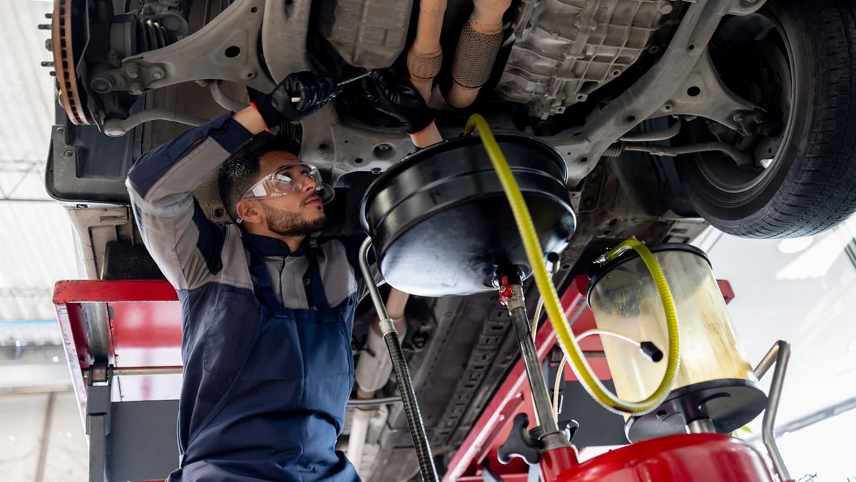 Technician draining transmission fluid from a vehicle on a lift